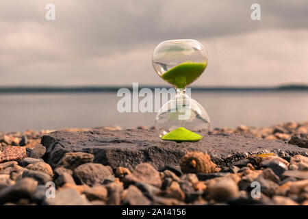 Avec Hourglass à sable vert sur le lac, se tenir sur les petites pierres. Concept de temps Banque D'Images