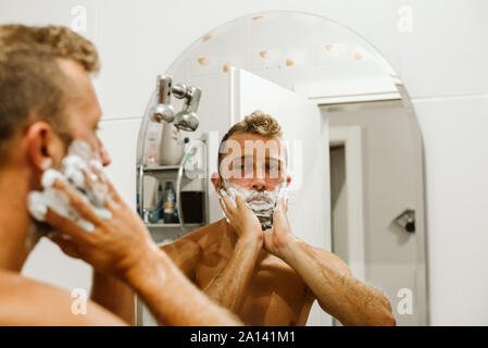 Man shaving face au miroir de salle de bains Banque D'Images