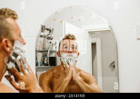 Man shaving face au miroir de salle de bains Banque D'Images