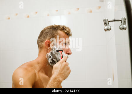 Man shaving face au miroir de salle de bains Banque D'Images