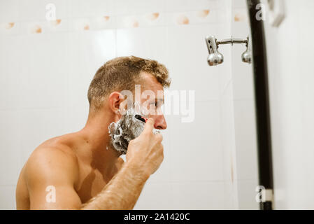 Man shaving face au miroir de salle de bains Banque D'Images