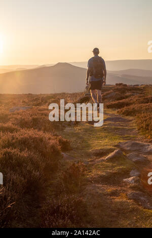 L'homme avec un sac à dos marche sur une piste que les landes Golden Sun est doté d'un paysage lointain de collines dans l'arrière-plan. Banque D'Images