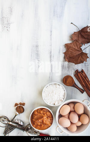 Ingrédients de purée de potiron, la farine, la cannelle et les oeufs brun avec l'automne les feuilles séchées sur un léger fond rustique. Ou de pain de potiron recette de muffins. Banque D'Images
