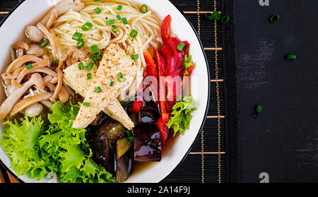Asian vegan nouilles potage au tofu, fromage et champignons shimeji aubergines frites dans un bol sur fond sombre. Vue d'en haut Banque D'Images