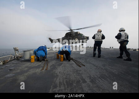 Les marins à bord de l'USS Ross se préparent à caler et la chaîne d'un hélicoptère Puma de la marine roumaine. Banque D'Images