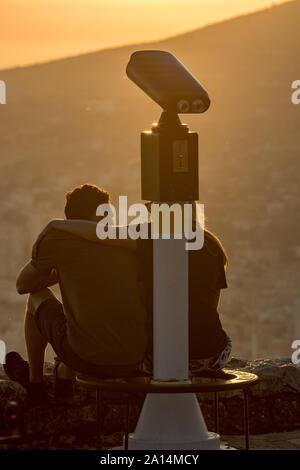 SARANDA, ALBANIE - 6 juin 2019 : en attente de la tombée de la couple méconnaissable, deux jeunes gens s'asseoir et d'accolade au coucher du soleil et admirer les magnifiques vues sur la ville albanaise derrière payé observation deck Banque D'Images