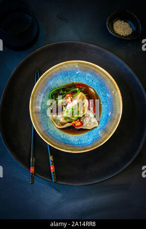 Boulettes asiatiques dans un bouillon avec les piments et baguettes sur fond sombre Banque D'Images