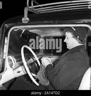 Chauffeur de taxi dans les années 50. Une femme chauffeur de derrière le volant dans son taxi. Elle est le tricot en attendant un client. La Suède 1958 Kristoffersson ref CC59-5 Banque D'Images