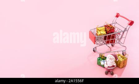 Concept d'achats de Noël, mini red shop panier trolley avec le Père Noël de jouets et de boîte-cadeau isolé sur fond rose pale, copie vierge de l'espace, Close up Banque D'Images