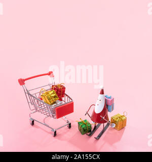 Concept d'achats de Noël, mini red shop panier trolley avec le Père Noël de jouets et de boîte-cadeau isolé sur fond rose pale, copie vierge de l'espace, Close up Banque D'Images