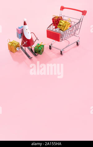 Concept d'achats de Noël, mini red shop panier trolley avec le Père Noël de jouets et de boîte-cadeau isolé sur fond rose pale, copie vierge de l'espace, Close up Banque D'Images