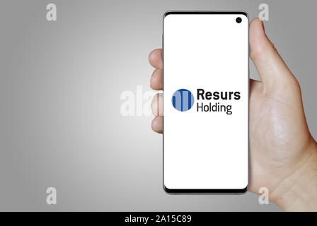Un homme est titulaire d'un smartphone affichant le logo de société Resurs Holding cotée sur OMX Stockholm. Dégradé de gris en arrière-plan. Credit : PIXDUCE Banque D'Images
