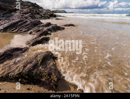 Marée montante sur la plage à Hayle Bay, Cornwall, Angleterre Royaume-uni sur une journée ensoleillée avec des rochers et des vagues. Banque D'Images