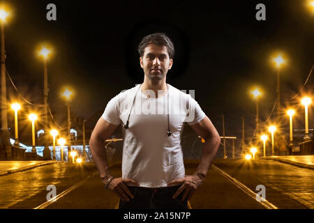 Jeune homme debout avec ses mains sur les hanches on city street at night Banque D'Images