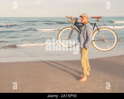 Homme nu debout avec Fixie vélo sur son épaule sur la plage Banque D'Images