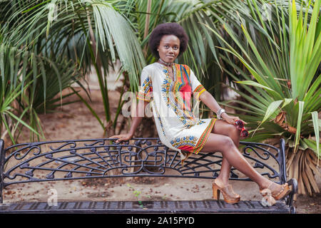 Jeune femme posant sur un banc parmi les plantes tropicales Banque D'Images