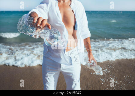 Homme debout en face de la mer de vider les bouteilles en plastique, close-up Banque D'Images