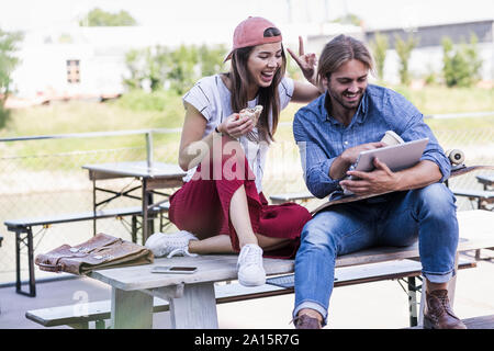 Young couple sitting on table dans un café en plein air à l'aide de tablet Banque D'Images