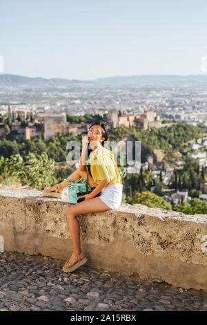 Jeune femme avec caméra assis sur un mur à l'Alhambra, Grenade, Espagne Banque D'Images