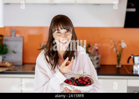 Portrait of happy woman wearing pyjamas manger des fruits dans la cuisine à la maison Banque D'Images