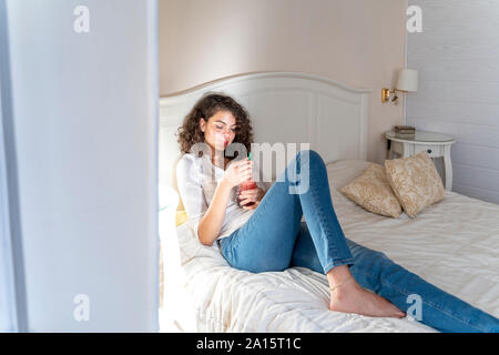 Jeune femme détendue lying on bed with boisson saine Banque D'Images
