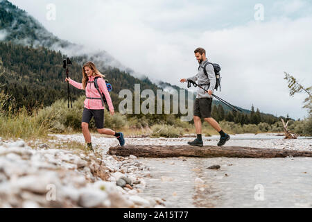 Jeune couple en randonnée crossing river sur un journal, Vorderriss, Bavière, Allemagne Banque D'Images