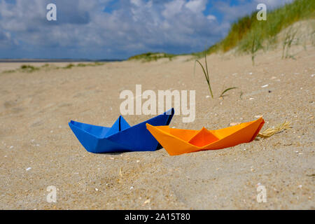 Bateau de papier bleu et orange dans le sable à la plage Banque D'Images