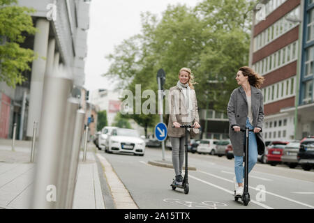 Les jeunes femmes équitation des scooters électriques dans la rue Banque D'Images