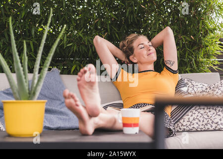 Relaxed woman sitting on couch sur terrasse à la maison en se penchant en arrière Banque D'Images