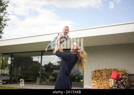 Heureuse mère soulevant baby girl en jardin de sa maison Banque D'Images