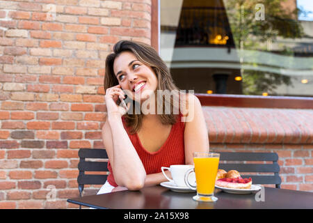 Portrait of smiling young woman on the phone assis au café de la rue Banque D'Images
