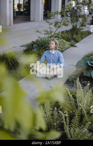 Jeune homme méditant outside office building Banque D'Images