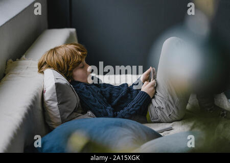 Redheaded boy lying on couch looking at cell phone Banque D'Images