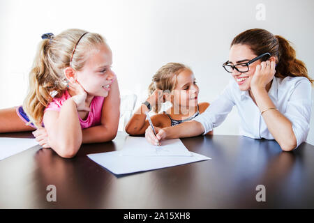 Happy teacher sitting at desk avec deux écolières écrit sur papier Banque D'Images