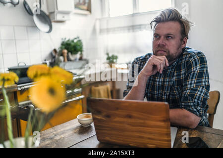 L'homme à l'aide de l'ordinateur portable sur une table de cuisine Banque D'Images