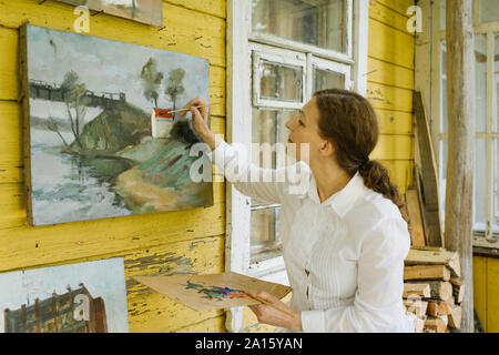 Sa peinture de finition peintre féminin à l'ancienne maison de village terrasse en bois Banque D'Images