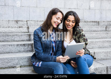 Happy young women watching tablet sitting on steps ensemble à Madrid, Espagne Banque D'Images