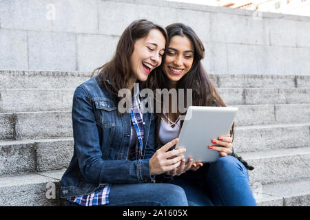 Happy young women watching tablet sitting on steps ensemble à Madrid, Espagne