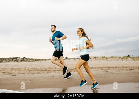Jeune couple jogging sur la plage Banque D'Images