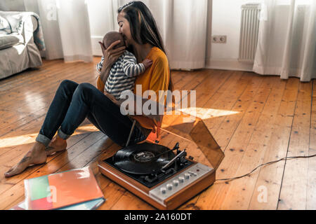 Mère avec bébé assis sur le plancher à la maison avec un record player Banque D'Images