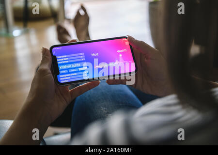 Jeune femme avec smartphone avec fonctions de contrôle smart home Banque D'Images