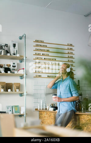 Young woman listening music, portant des écouteurs, standing in coffee shop Banque D'Images