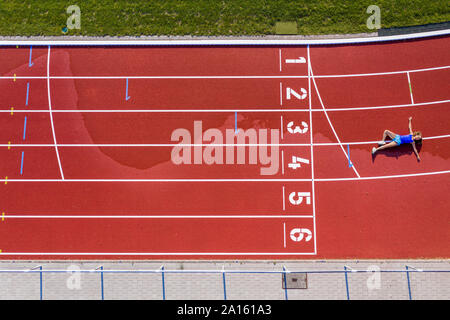Vue aérienne d'un jeune athlète féminin allongé sur une piste en tartan après avoir franchi la ligne d'arrivée Banque D'Images