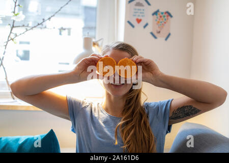 Jeune femme espiègle couvrant ses yeux avec des oranges à la maison Banque D'Images