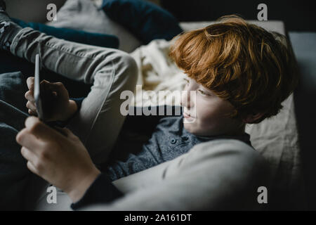 Redheaded boy lying on sofa using digital tablet Banque D'Images