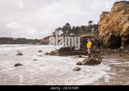 Woman Veste pluie jaune debout sur rock à la plage Banque D'Images