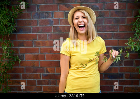 Portrait of laughing young woman standing à un mur de briques Banque D'Images