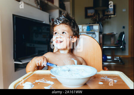 Petit garçon assis dans une chaise haute, manger le petit déjeuner à la maison Banque D'Images