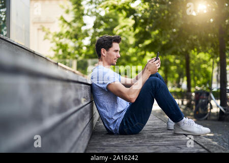 Man sitting on bench using smartphone Banque D'Images