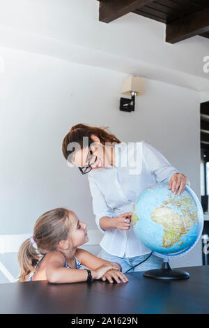 Smiling teacher et lycéenne sitting at desk with globe Banque D'Images